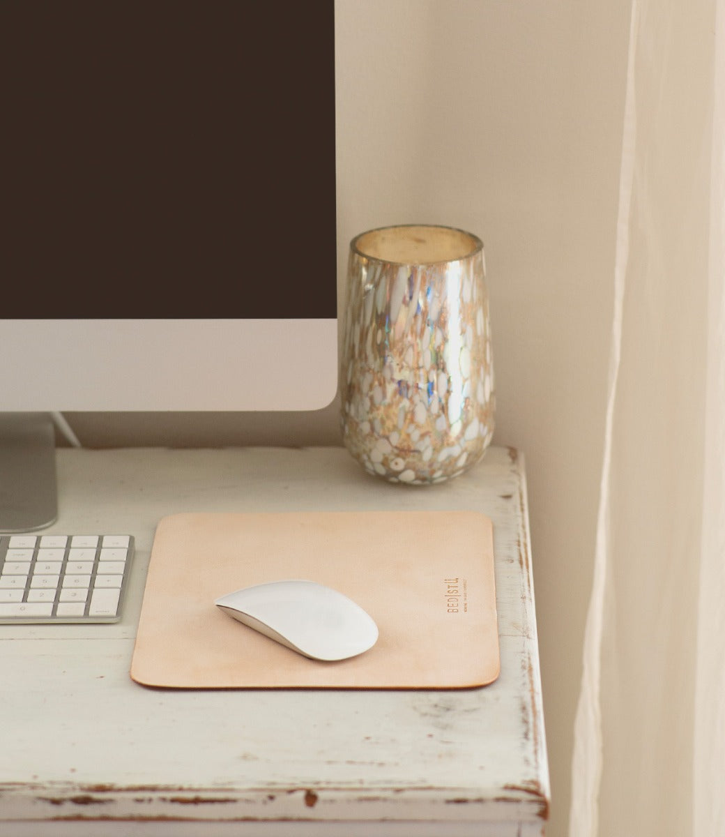 A computer monitor, keyboard, and mouse sit on a white desk next to a marbled glass candle holder, complemented by the Launcher Mouse Pad from Bed|Stü, which elevates this workspace accessory setup.