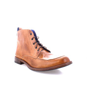 The Bed|Stü Lincoln II is a brown leather lace-up ankle boot featuring an apron toe, low heel, dark sole, and blue inner lining, displayed against a white background. This stylish men's boot effortlessly combines work-boot durability with modern design.