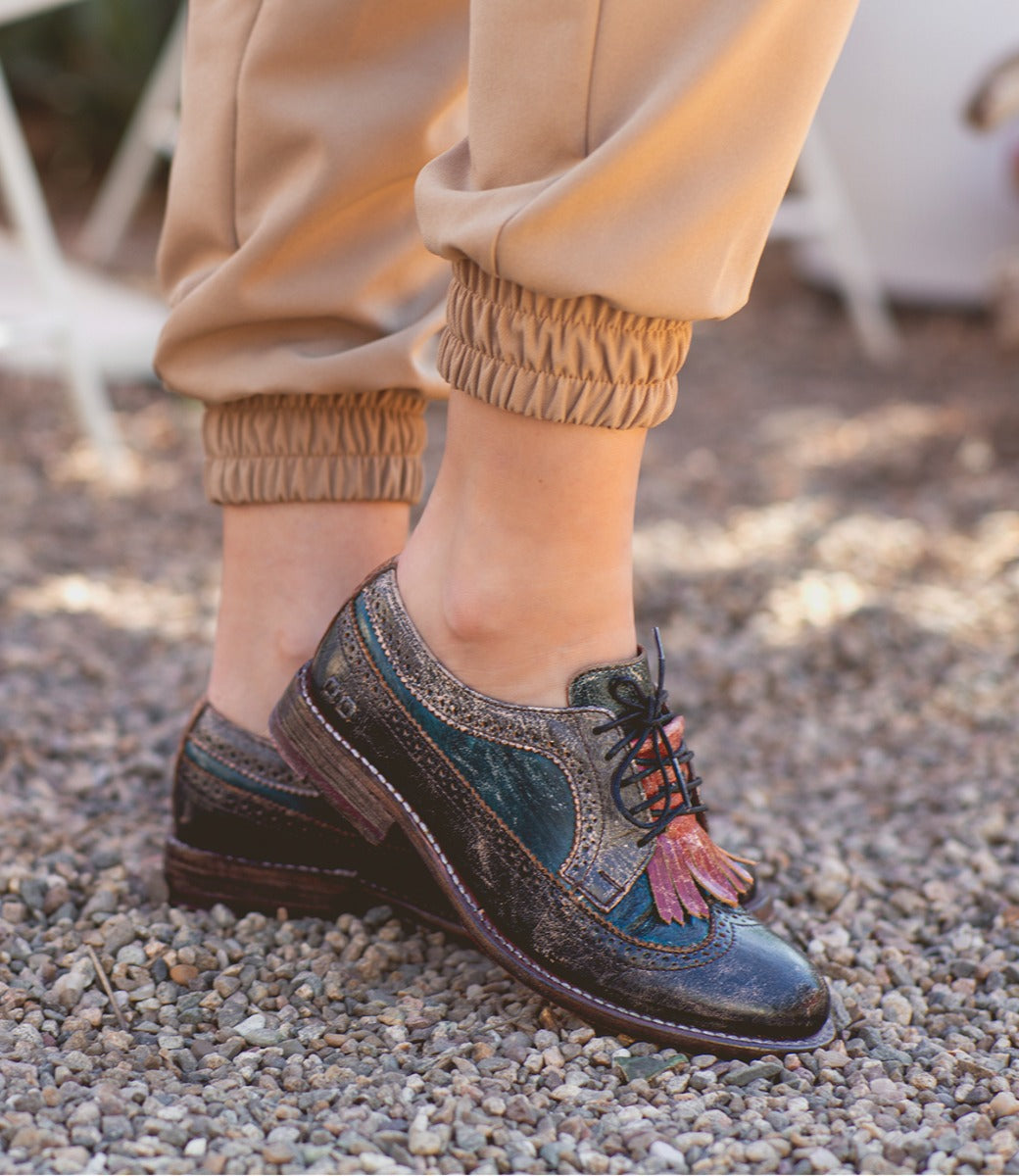 Wearing tan jogger pants and the Bed|Stü Lita K vintage-style leather lace-up shoes featuring brogue details and a wingtip toe, standing on gravel.