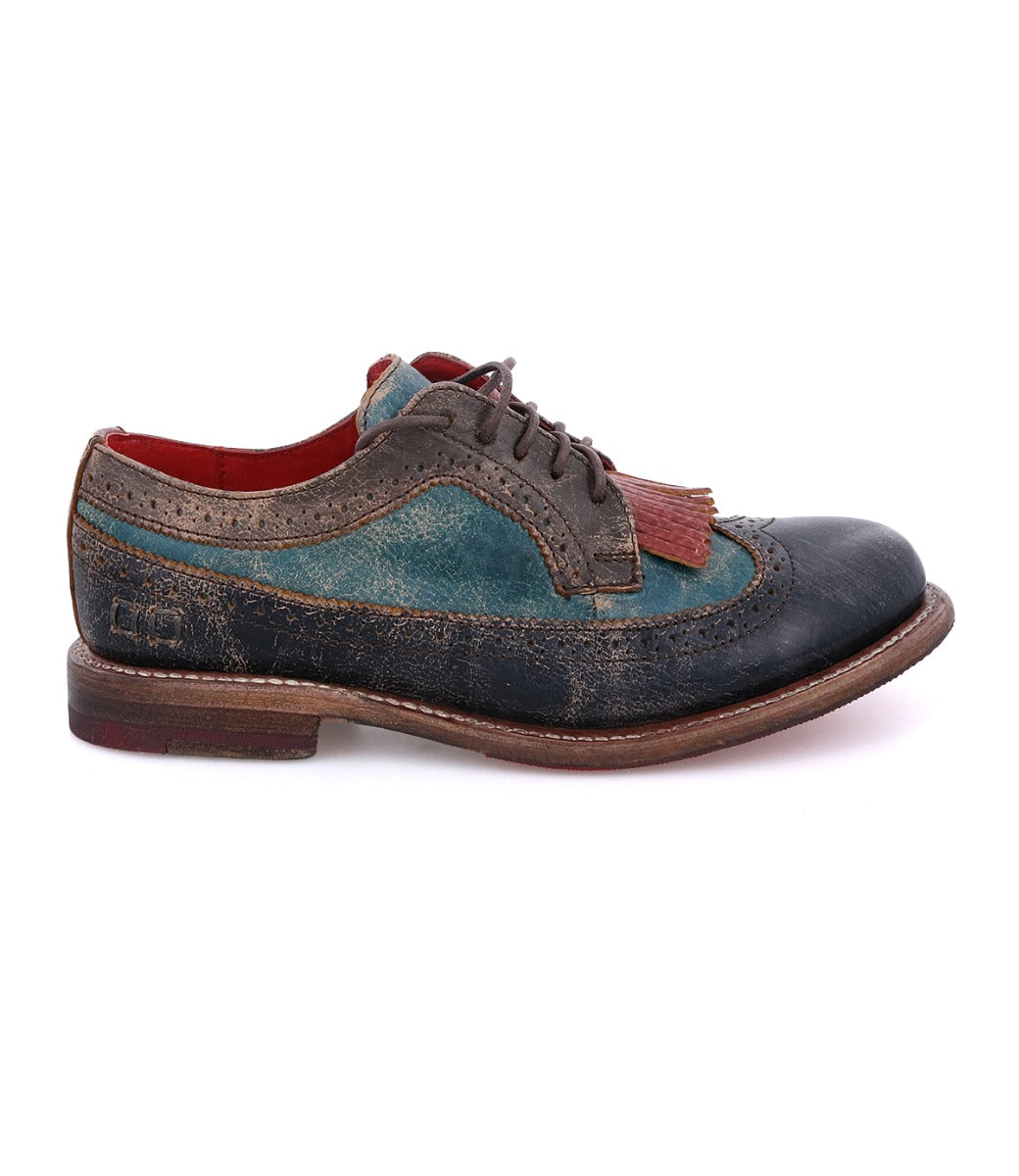 A worn, multicolored leather oxford shoe with brogue details and a classic wingtip toe from Bed|Stü, the Lita K features a red interior lining and a decorative brown fringe on top, shown in a side profile view.
