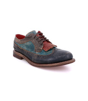 The Bed|Stü Lita K dress shoe, featuring blue, brown, and red leather accents, a wingtip toe with decorative brogue details, and a fringe detail over the laces, is displayed on a white background.