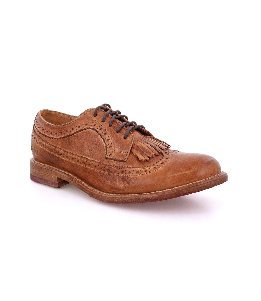 The Bed|Stü Lita K is a brown leather brogue dress shoe featuring classic brogue details, decorative perforations, black laces, a fringe detail on the upper, and a stylish wingtip toe, displayed on a white background.