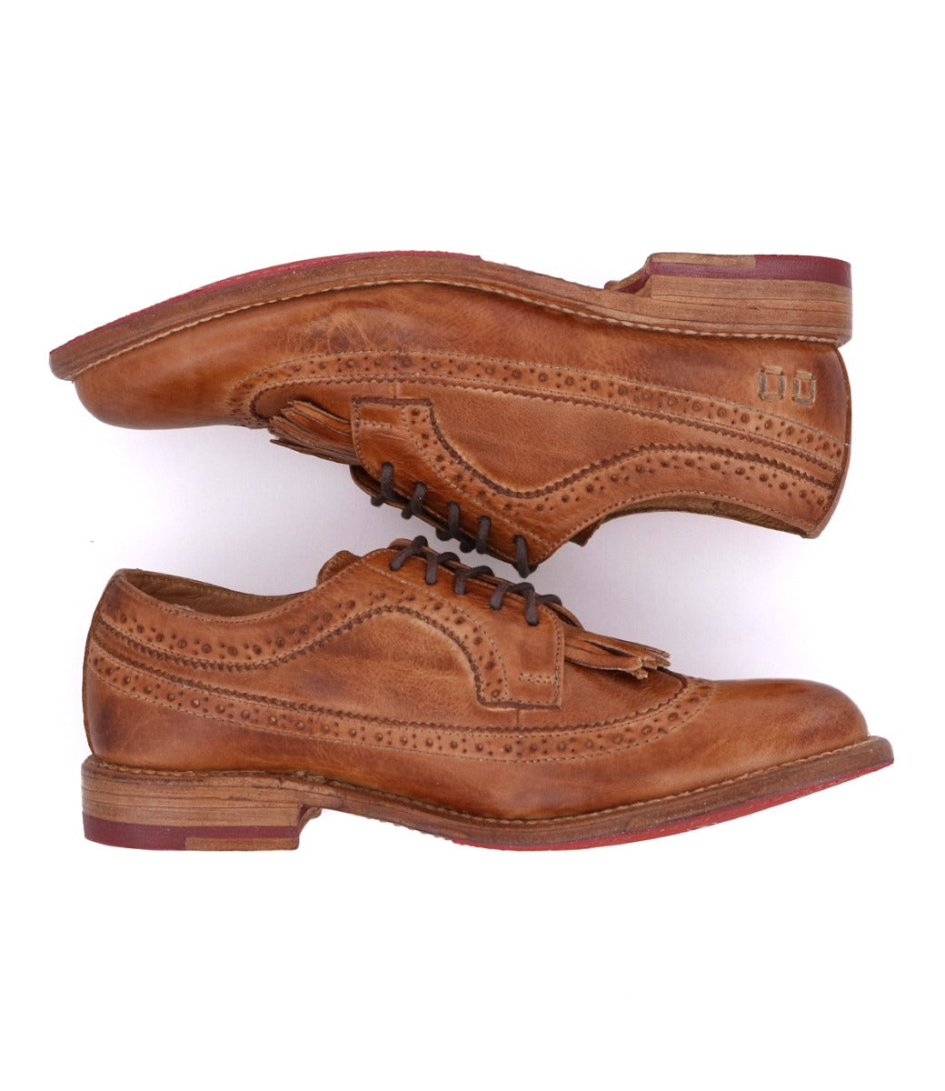 A pair of Bed|Stü Lita K brown leather brogue dress shoes with laces, stacked sole-to-sole, showcasing a classic wingtip toe, intricate brogue detailing, and eye-catching red accents on the soles.