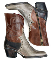 The Bed|Stü Locate boots are a pair of leather Western-style boots featuring brown, tan, and black color sections, decorative flame stitching, metal studs, a side zipper, and low heels.