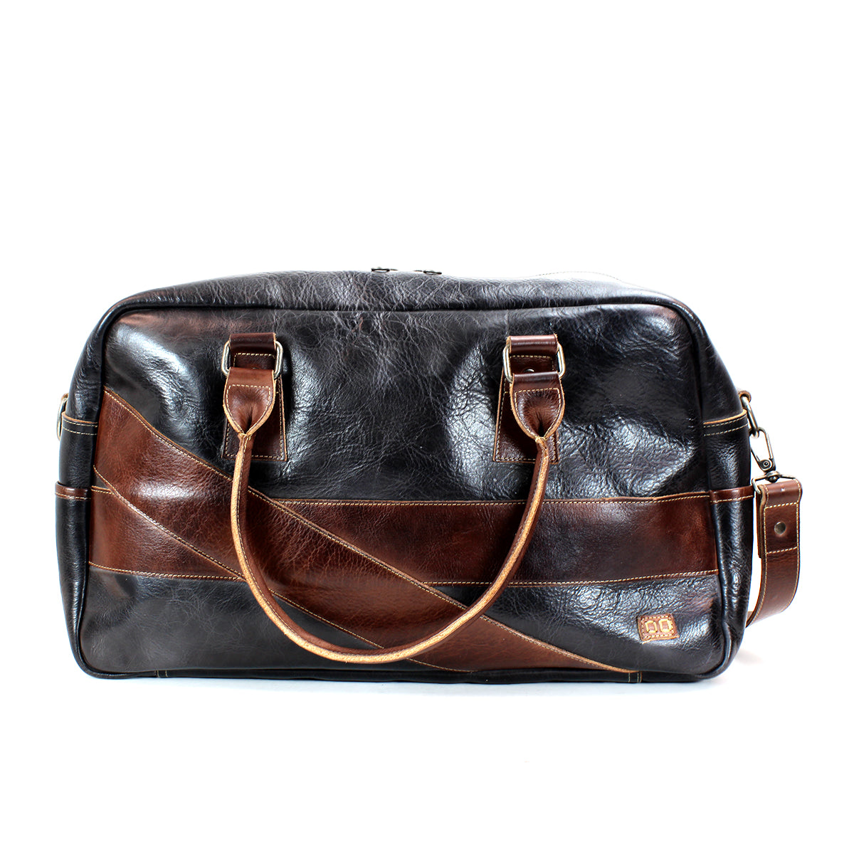 The Luke by Bed|Stü is a black and brown oversized duffle bag crafted from vegetable-tanned leather, featuring dual handles, a shoulder strap, and a small logo patch on the front—perfect as a stylish travel bag.