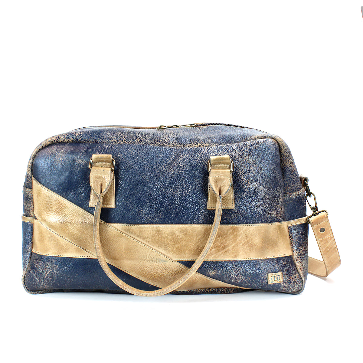 The Luke travel bag by Bed|Stü is an oversized duffle crafted from vegetable tanned leather in blue and tan. Featuring dual handles, a detachable shoulder strap, and a bold diagonal tan stripe, this stylish bag is presented against a white background.