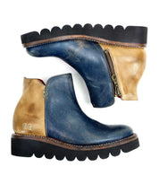 A pair of Bed|Stü Lydyi leather ankle boots featuring blue and tan leather panels, side zippers, brown midsoles, and black platform outsoles with scalloped edges and cushioned insoles for added comfort; displayed side by side on a white background.