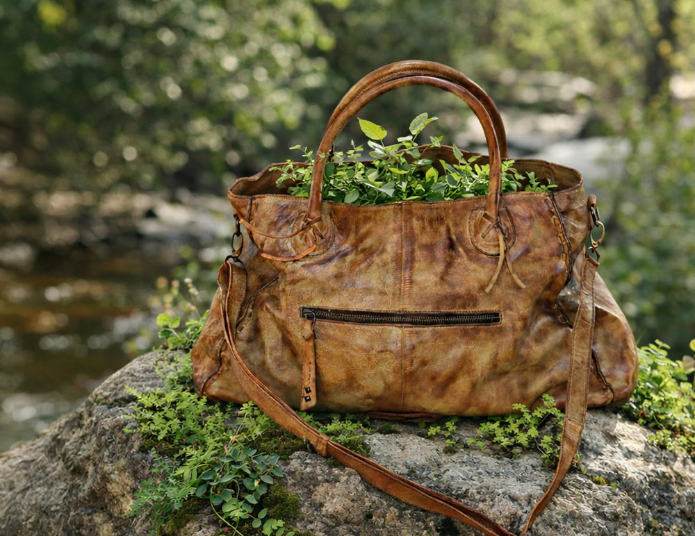 Brown leather handbag filled with green plants, resting on a mossy rock beside a stream.