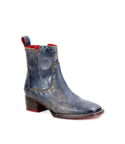 The Bed|Stü Merryli ankle boot is shown in blue distressed leather with a block heel, red interior lining, and a convenient pull tab, displayed on a white background. This stylish boot highlights meticulous hand-stitched details and a modern square toe design.