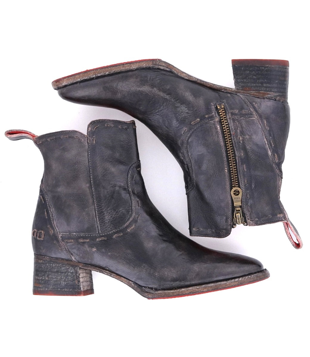 The Merryli boots from Bed|Stü are a pair of distressed black leather, square-toe boots featuring side zippers, low heels, red pull tabs, and visible hand-stitched detailing. Prominent stitching adds to their bold, modern look.