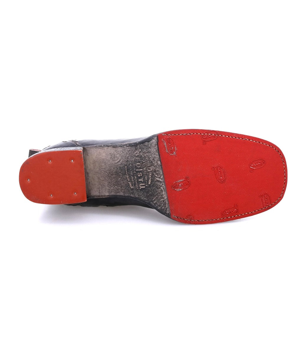The bottom view of the Bed|Stü Merryli black leather boot showcases its red textured sole, visible stitching, and heel with metal studs, emphasizing the craftsmanship that defines these hand-stitched boots.