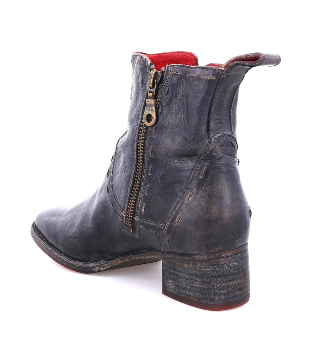 The Bed|Stü Merryli is a hand-stitched black leather ankle boot with a side zipper, stacked heel, and visible red lining. Photographed from the back left angle, these expertly crafted boots showcase timeless style.