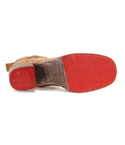 The Merryli boot by Bed|Stü, crafted from tan leather and inspired by classic hand-stitched designs, is pictured upside down to showcase its vibrant red sole and heel, complete with visible stitching and nail marks.