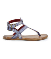 The Bed|Stü Moon sandal is a single flat design featuring metallic purple leather straps, dual brass ankle buckles, a cushioned insole, brown sole, and back ankle support, shown in profile on a white background.