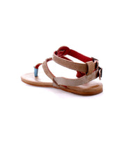 The Bed|Stü Moon is a tan and red open-toe leather sandal featuring ankle and heel straps, a buckle closure, a thin flat sole, and a cushioned insole, displayed against a white background.