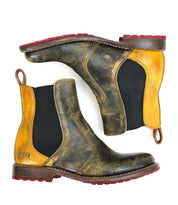 Introducing the Bed|Stü Nandi—a pair of leather Chelsea boots featuring a striking black and yellow distressed finish, black elastic side panels, red pull tabs, bold red rubber soles, and classic brown midsoles. With their timeless slip-on design, the Nandi boots are versatile footwear essentials suited to any occasion.