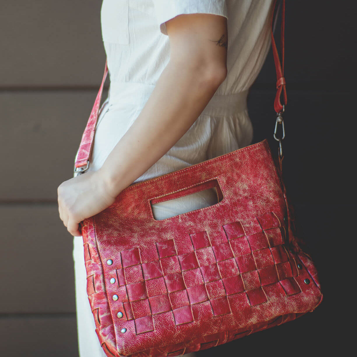 A person dressed in white carries the Bed|Stü Orchid bag—a handwoven leather accessory with a built-in handle, modern timeless design, and metal rivet accents.