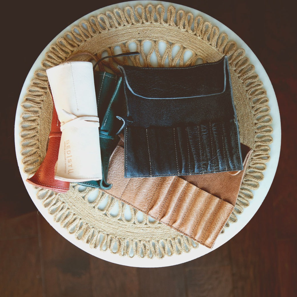 Bed|Stü’s Prepped Leather Wraps are stylish leather organizers, perfect for artists, displayed on a woven placemat atop a round white table.