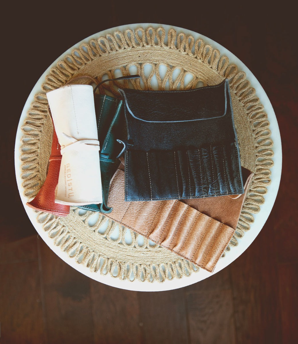Bed|Stü’s Prepped Leather Wraps are stylish leather organizers, perfect for artists, displayed on a woven placemat atop a round white table.
