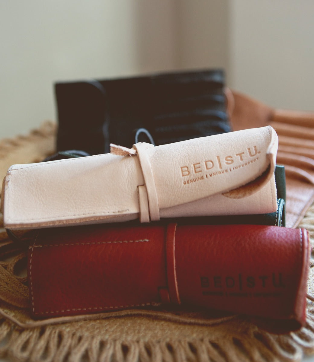Stack of three Prepped Leather Wraps by Bed|Stü in light pink, dark, and red—an ideal organizer for artists. The light pink wrap features "BED STU" embossed on it.