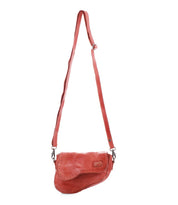 The Bed|Stü Priscilla is a small red leather crossbody bag with an adjustable strap and flap closure, shown against a plain white background. This versatile style can be worn as either a crossbody or waist bag.