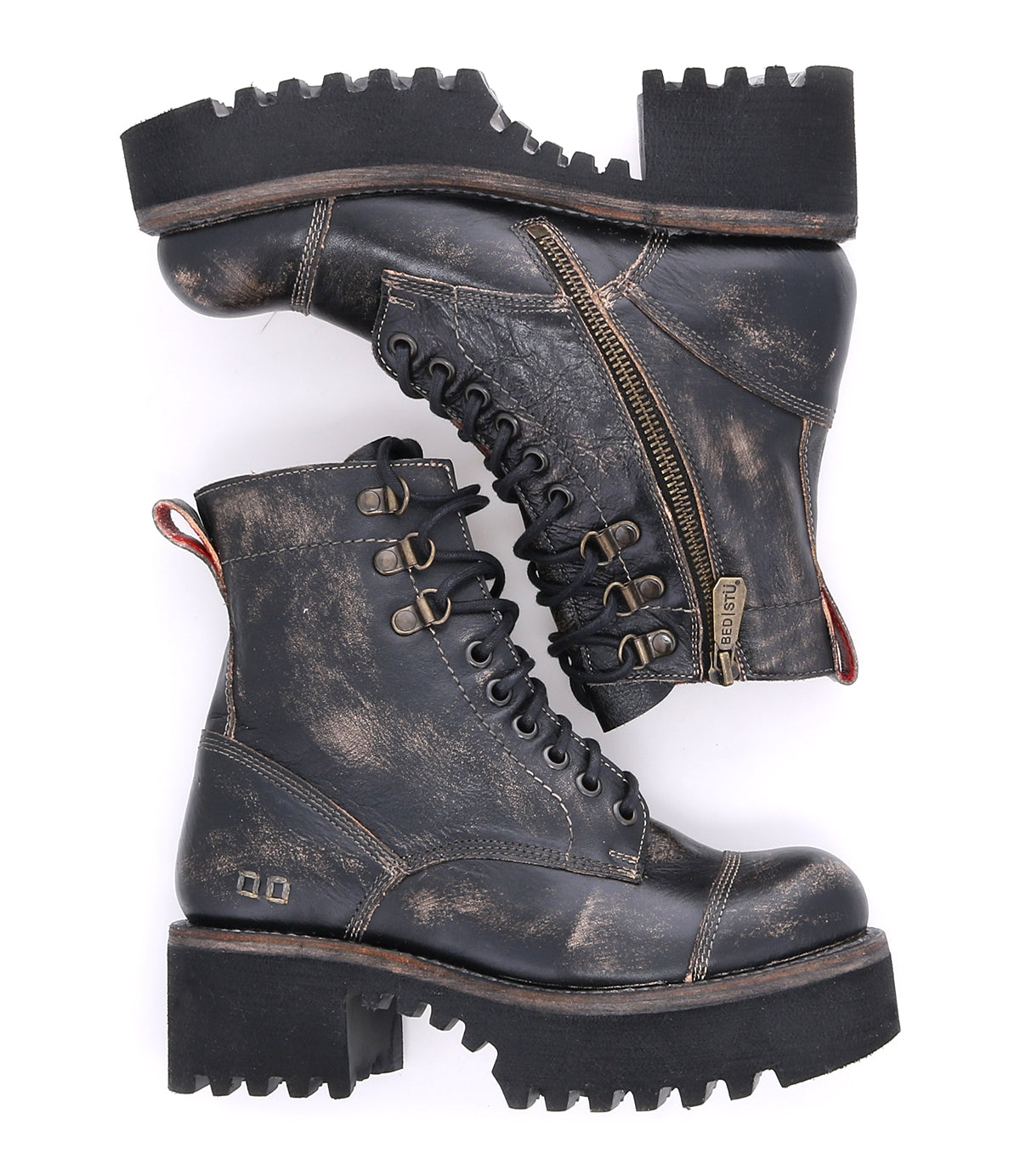 A pair of Bed|Stü Prudence Hi distressed black leather combat boots with thick lug soles, a chunky platform outsole, metal eyelets, side zippers, and a red pull tab at the heel are displayed against a white background—perfect for those seeking truly edgy boots.