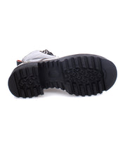The Bed|Stü Prudence Hi, a black leather combat boot, is shown lying on its side against a white background, highlighting its chunky platform outsole and deeply textured rubber sole.