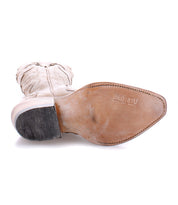 A tan Bed|Stü Queen Western boot is shown sole-up; the sole features branding and visible wear, along with detailed stitching and a stacked heel.