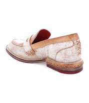 The Reina by Bed|Stü is a tan and off-white leather penny loafer featuring visible stitching, decorative lacing at the heel, a leather upper, and a distinctive red sole.