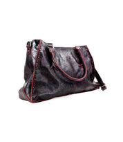 The Bed|Stü Rockaway is a black full-grain leather tote bag featuring red trim, silver hardware, two handles, and a detachable shoulder strap—thoughtfully designed for everyday use and showcased against a white background.
