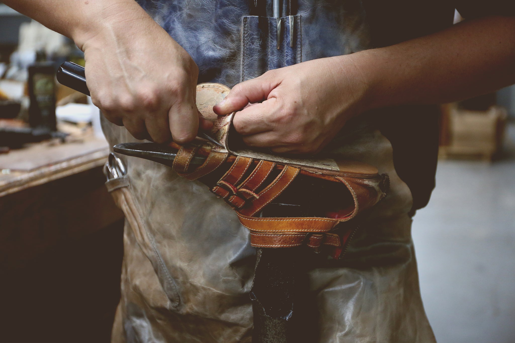 Craftsperson repairing a brown leather sandal by hand in a workshop.