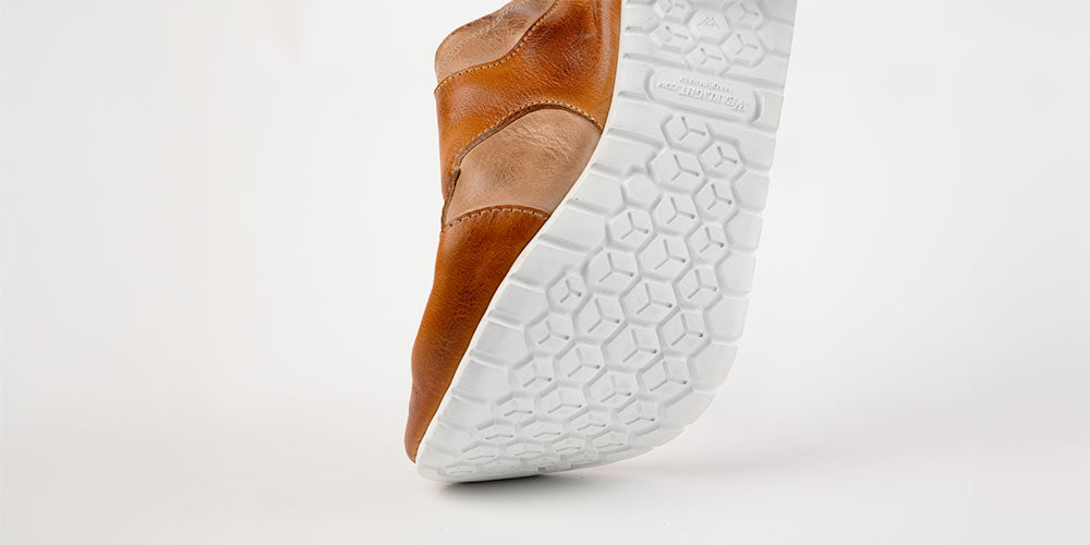 Close-up of a brown leather shoe showing its thick white treaded sole.