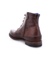 The Bed|Stü Spiker is a brown leather ankle boot with a lace-up design and side zipper, featuring a rugged sole, cushioned insole, and slightly worn finish, shown from the back angle on a plain white background.