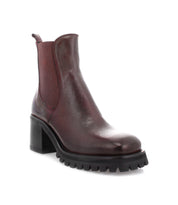 The Bed|Stü Surge is a dark red Italian leather Chelsea boot featuring a square toe, block heel, black lug sole, and side elastic panels, displayed at a three-quarter angle on a white background.