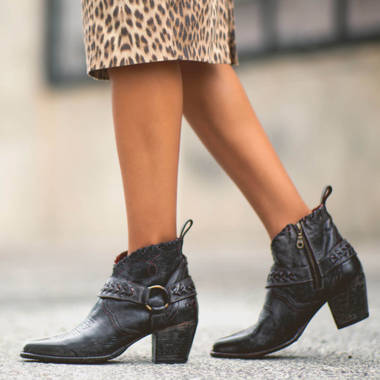 A person wearing a leopard print skirt and the Tania black vintage leather cowboy bootie by Bed|Stü, walking on a city street.