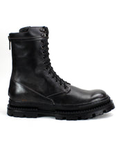 The Tempt boot by Bed|Stü is a black leather lace-up combat boot with a thick, rugged sole and a convenient side zipper, shown in profile on a white background—this stylish hybrid fuses classic combat and Chelsea boot details for versatile appeal.