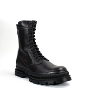 The Bed|Stü Tempt is pictured against a plain white background, showcasing its stylish hybrid design that combines elements of a classic combat boot and a Chelsea boot, featuring black leather, lace-up detailing, and a thick, rugged sole.
