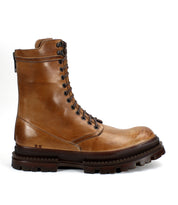 Bed|Stü's Tempt boot is a tan leather lace-up combat style featuring metal eyelets, a side zipper, and a thick, rugged dark brown sole—a stylish hybrid that fuses classic combat utility with the refined silhouette of a Chelsea boot, presented against a white background.