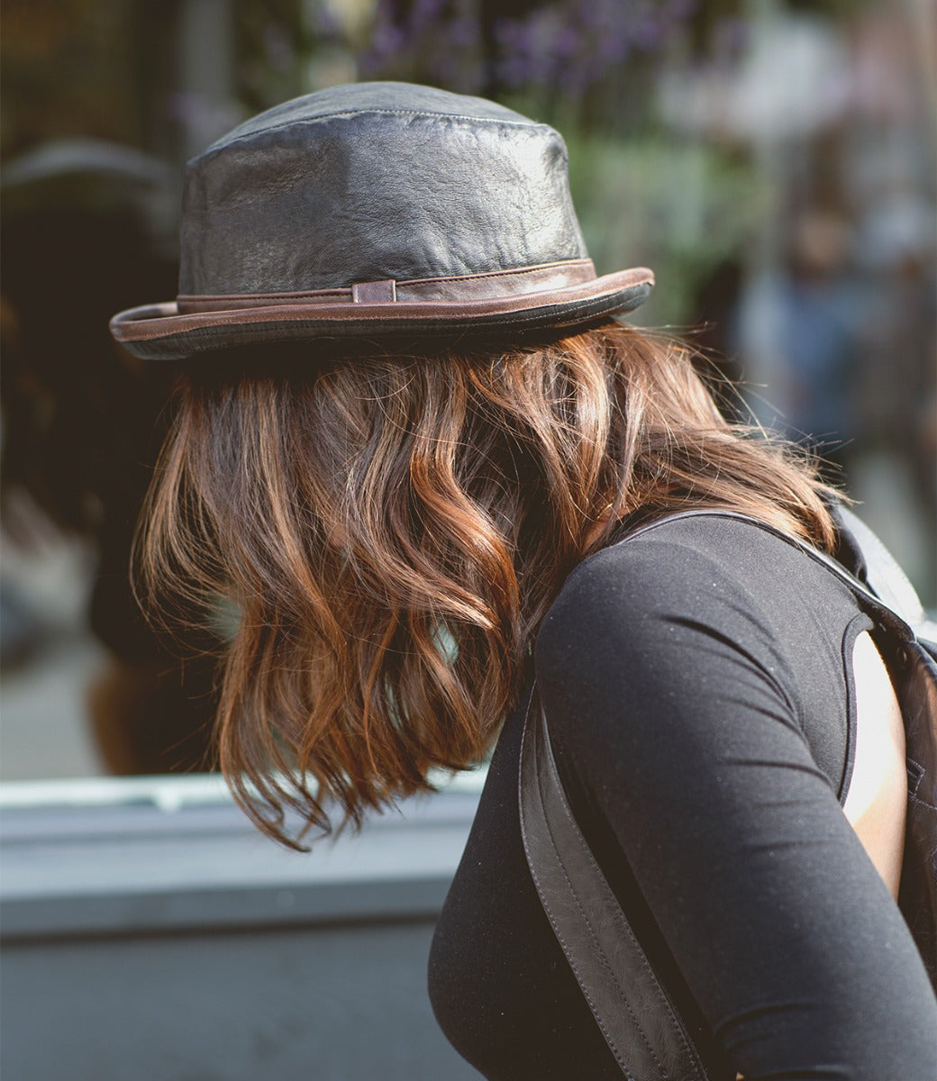 A person with wavy brown hair, wearing the Bed|Stü Turino lightweight black hat and a black top, is facing away from the camera outdoors.