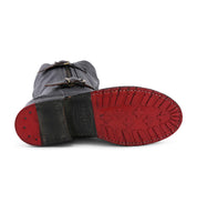 The Bed|Stü Gogo Lug Wide Calf boot is displayed sole-up, highlighting its black leather construction, red rubber tread, metal-studded heel, and visible buckles with stitching details for a rugged look.