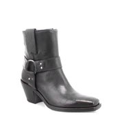 The Bed|Stü Vamoose is a black Italian leather ankle boot with a low heel, side buckle strap, decorative stitching, and a pointed toe in a modern harness-boot style, displayed against a white background.
