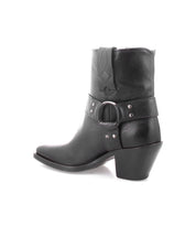 Introducing the Vamoose by Bed|Stü—a black Italian leather ankle cowboy boot featuring a pointed toe, chunky heel, and a decorative harness strap with metal ring and studs, showcased on a white background. This harness-boot style brings bold character to the classic silhouette.