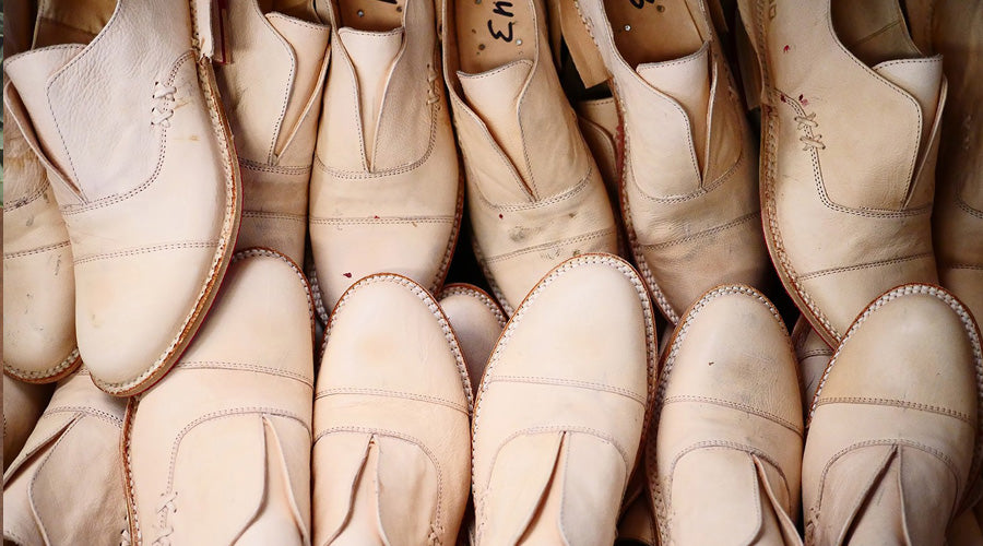 Rows of unfinished light-colored leather shoes stacked together, showing stitched uppers and raw leather edges.