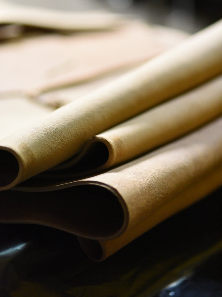 Close-up of rolled and folded tan leather pieces showing soft texture and raw edges.