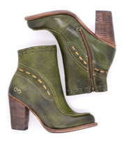 The Yuno ankle boots by Bed|Stü feature green leather uppers, brown wooden heels, decorative stitching, contrasting leather accents, convenient side zippers, and a subtle metallic logo on the heel area. Displayed against a white background.