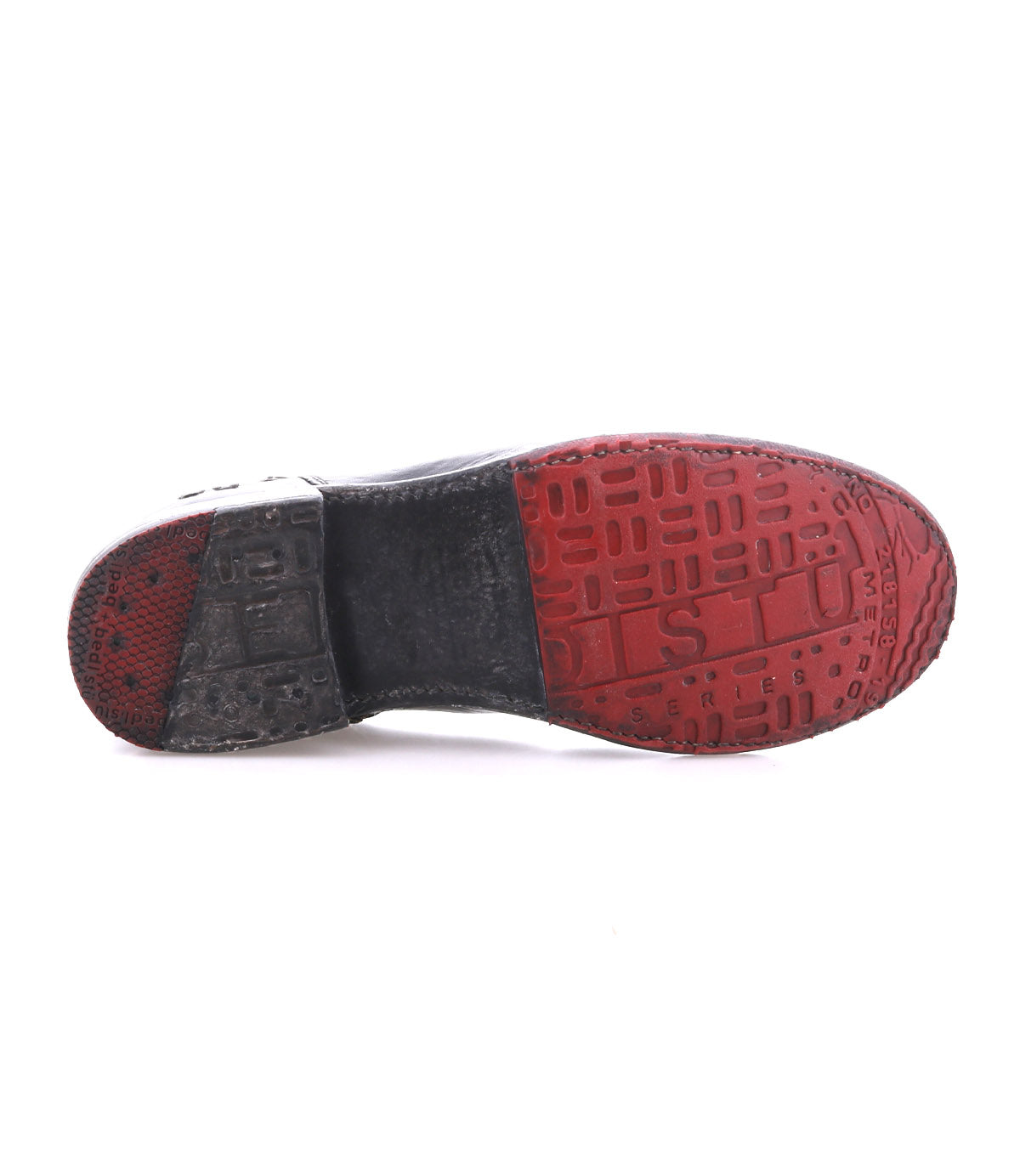 Bottom view of a single Yurisa black ankle boot by Bed|Stü, featuring a handcrafted two-tone sole with red and black tread, raised letters, and textured patterns that highlight its quality craftsmanship.