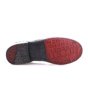 Bottom view of a single Yurisa black ankle boot by Bed|Stü, featuring a handcrafted two-tone sole with red and black tread, raised letters, and textured patterns that highlight its quality craftsmanship.