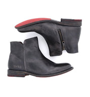 Pair of Bed|Stü Yurisa black leather ankle boots with side zippers, stacked wooden heels, and signature red outsoles, showcasing a durable leather outsole and meticulous handcrafted construction; displayed from the side and bottom on a white background.