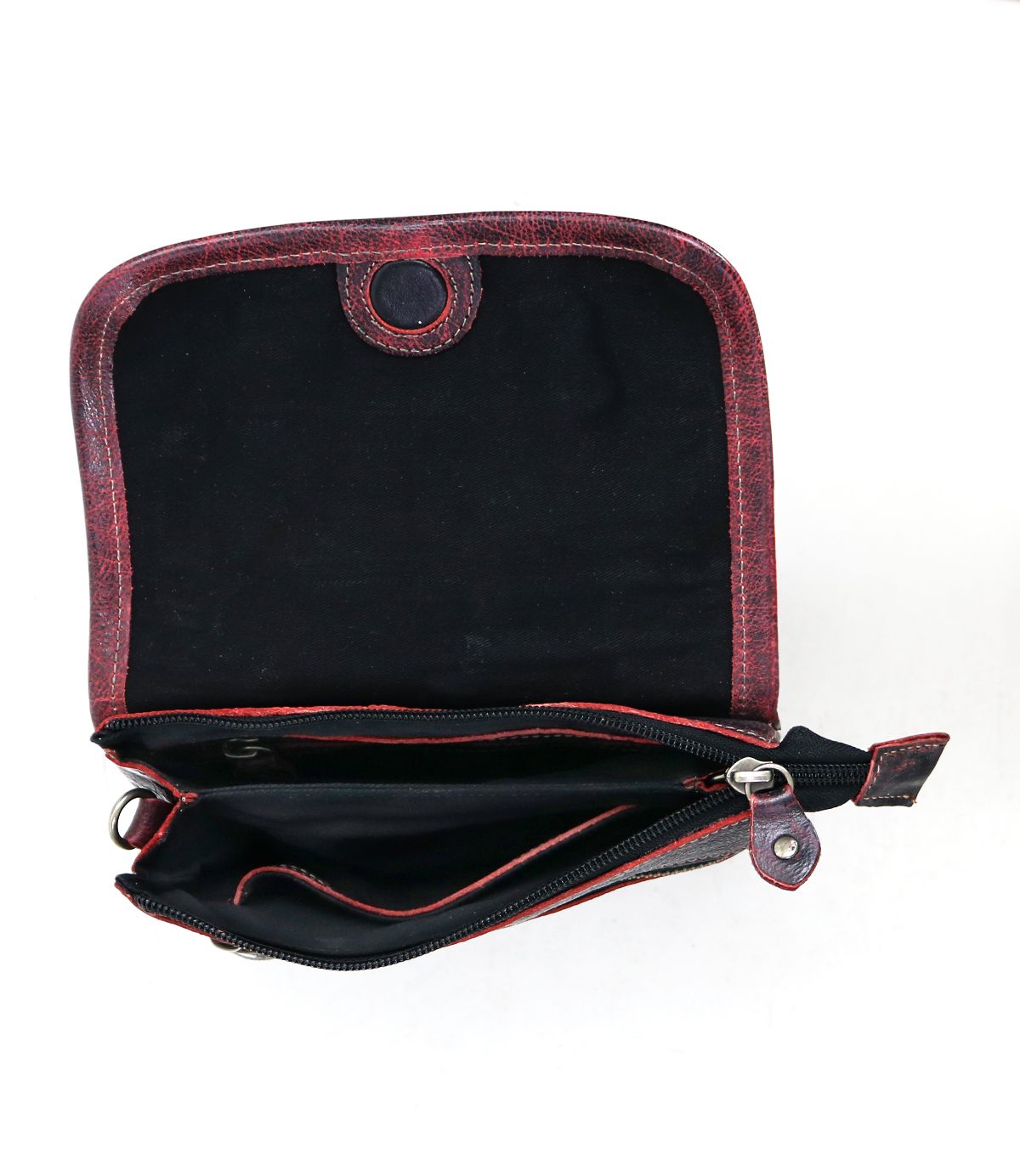 The Bed|Stü Ziggy is a small, red crossbody bag crafted from supple leather, shown with the flap open to reveal a black interior, a zippered pocket, and a button closure.
